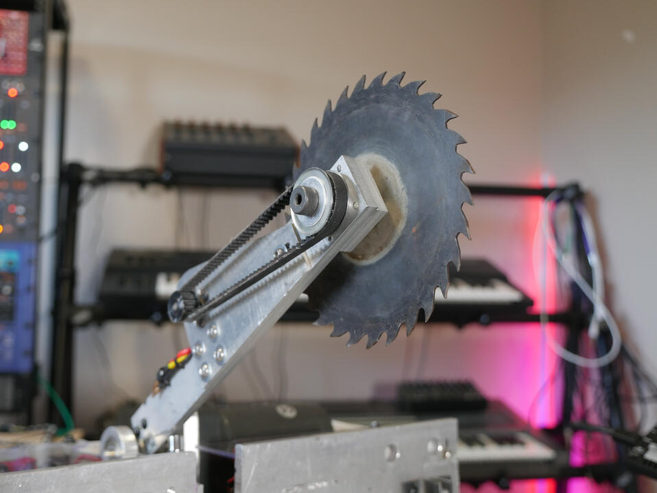 Larger combat robot in Makers Muse studio, metal beetleweight-class. Close up shot of a big sharp looking metal spinner blade, set on the end of a long arm.